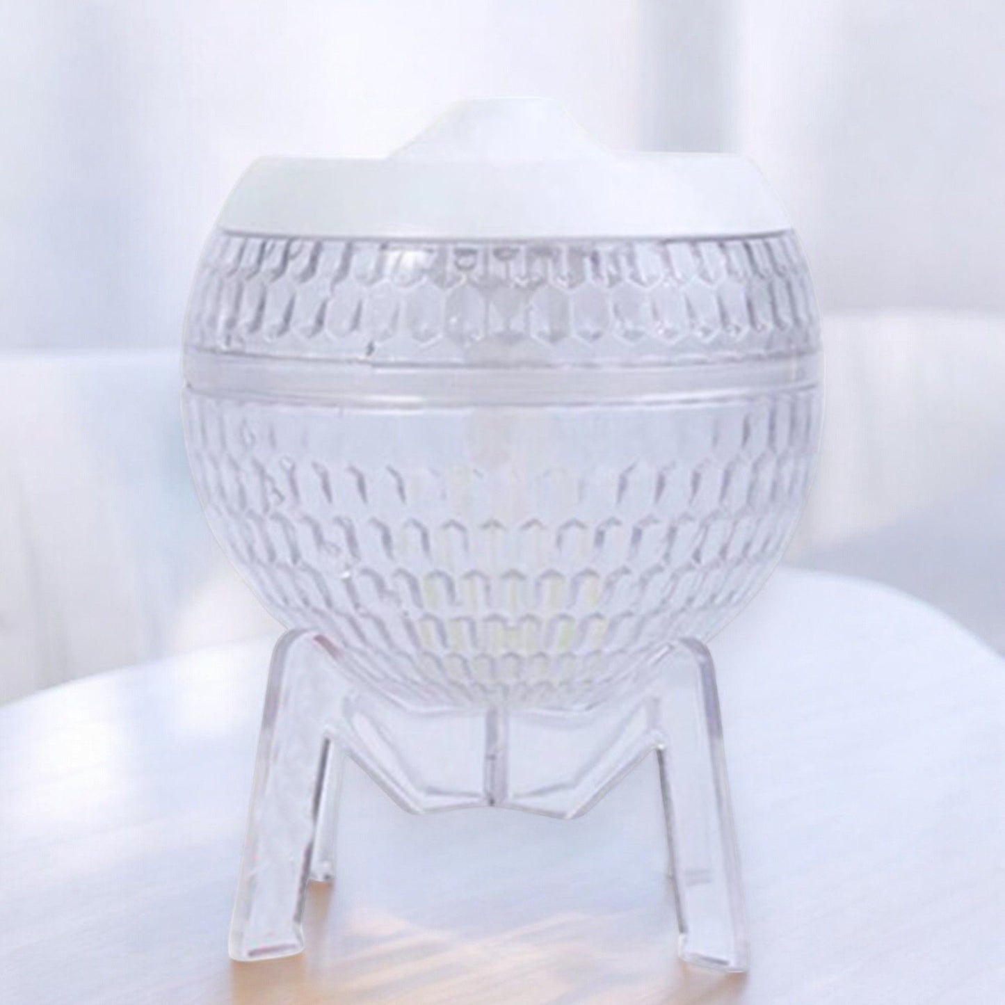 Difusor de aromas esférico y transparente, con textura de panal, base de trípode y tapa blanca. Diseño tipo planeta.