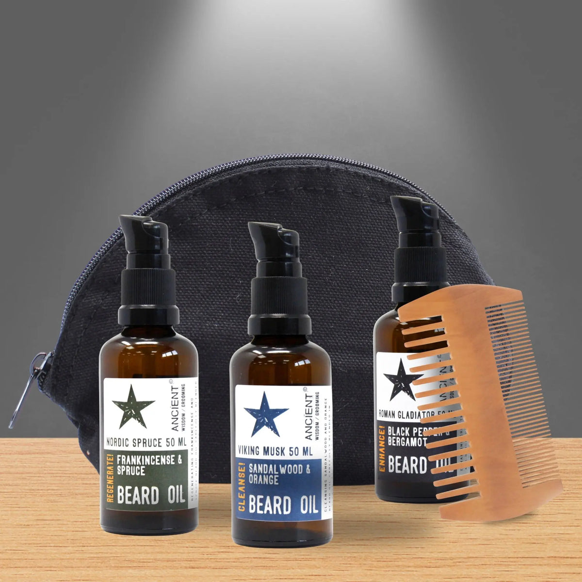 Set de regalo Ancient Wisdom: tres aceites para barba en frascos oscuros, un peine de madera y neceser negro sobre mesa.