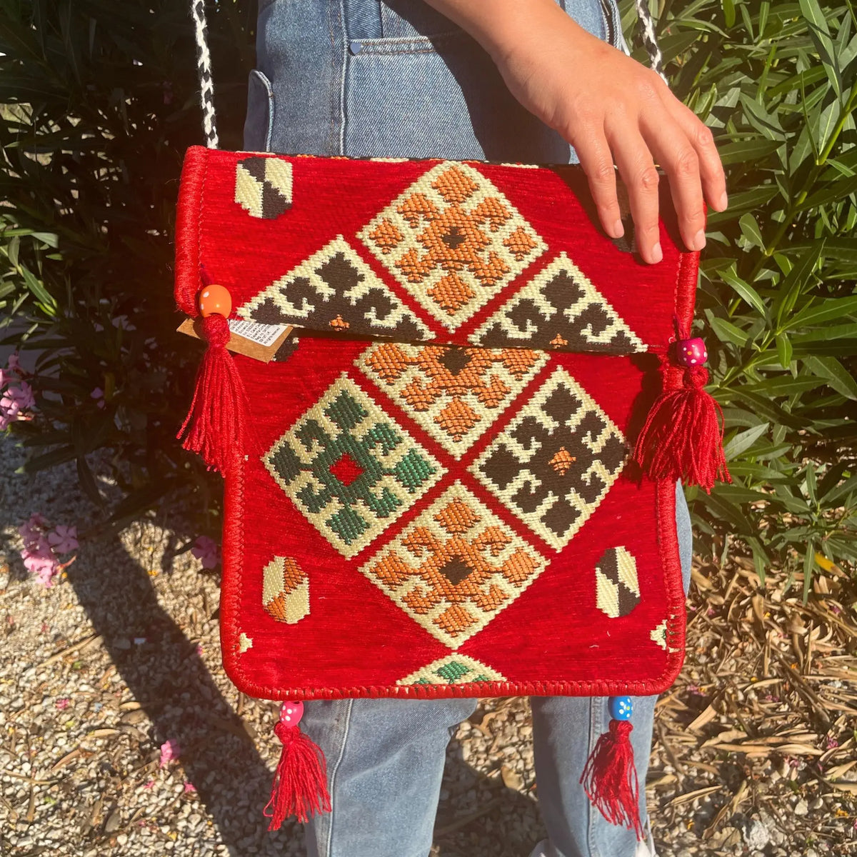 Bolso bandolera rojo de estilo artesanal con motivos geométricos bordados, borlas decorativas y correa trenzada bicolor