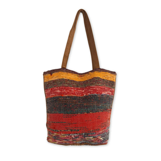 Bolso tote de tela reciclada con franjas tejidas en tonos atardecer: amarillo, rojo, negro y naranja, con asas cafés.