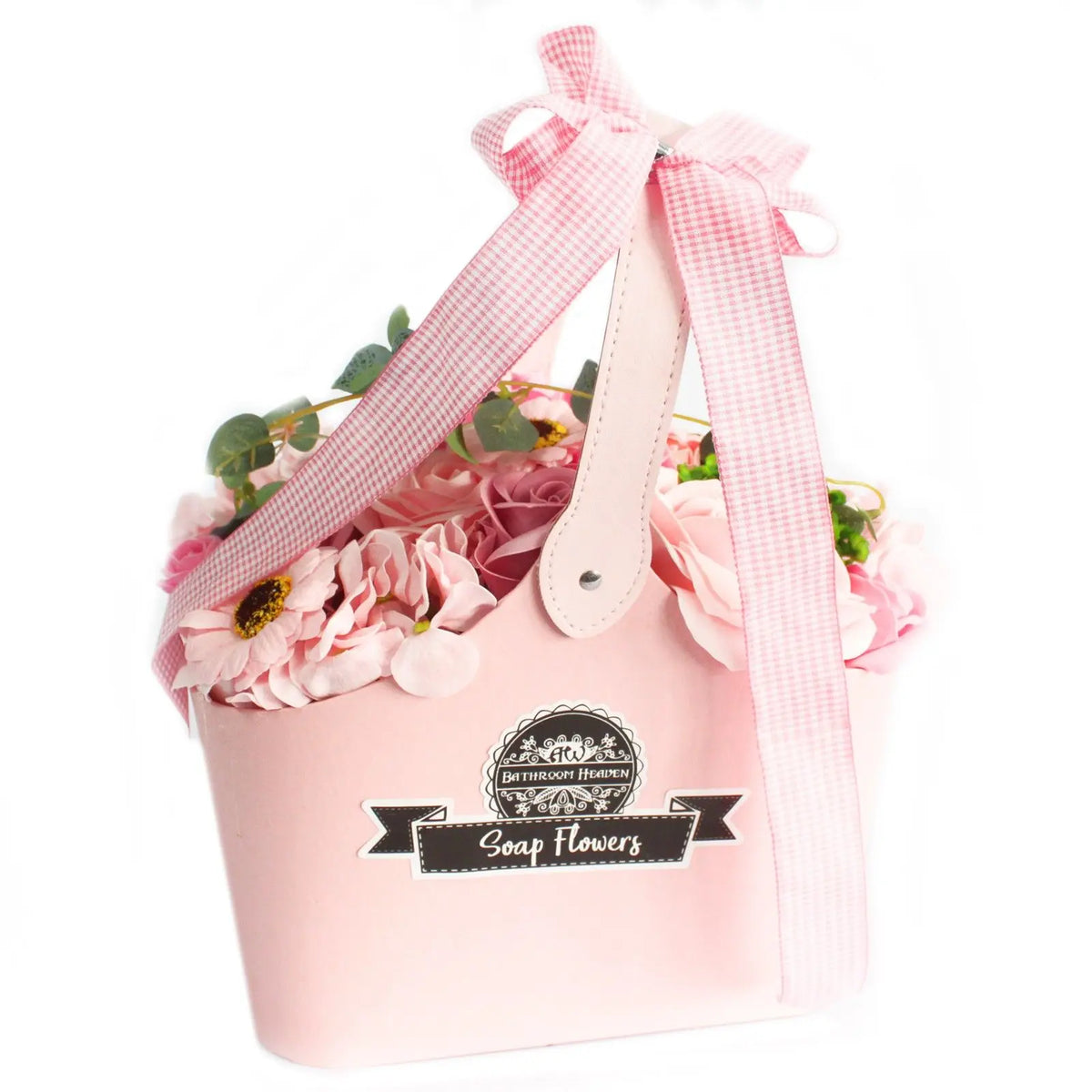 Cesta rosa con flores de jabón en tonos rosados y follaje verde, decorada con un lazo de tela a cuadros sobre fondo blanco.
