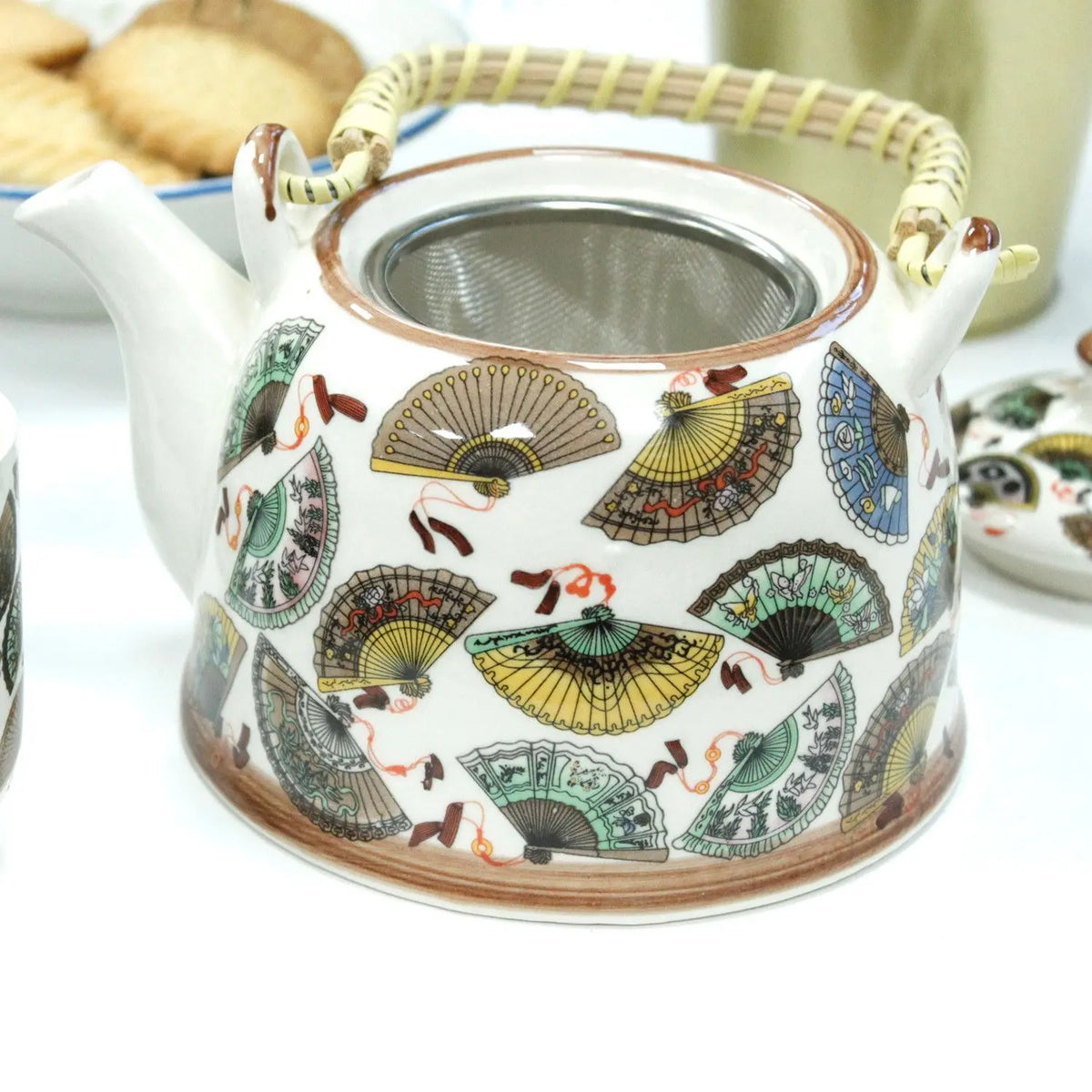 Tetera de cerámica blanca con diseño de abanicos chinos coloridos, colador metálico y asa de mimbre tejida artesanal