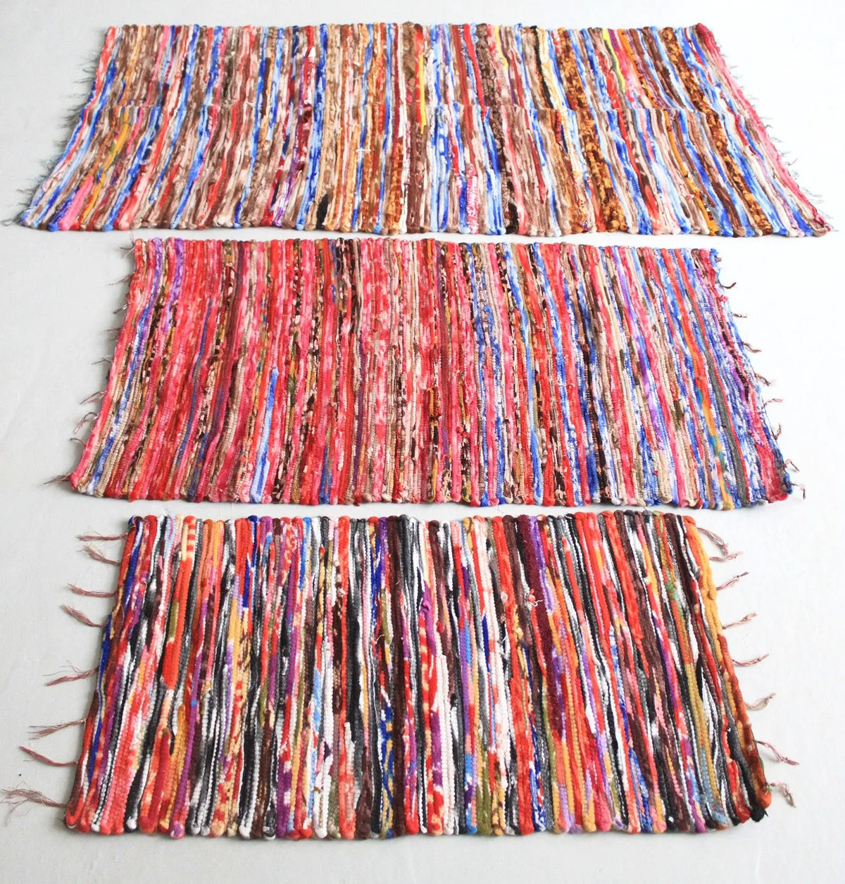 Tres alfombras rectangulares de trapo hechas a mano con tiras de tela multicolor en tonos vivos y estilo bohemio.