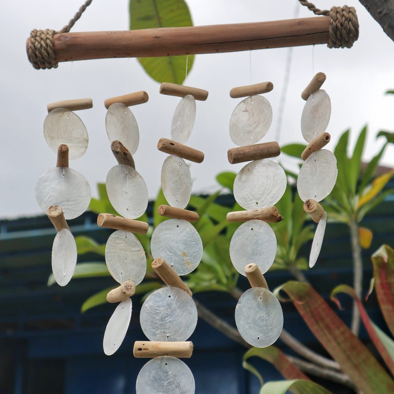 Carillón de madera flotante con discos de concha nácar blanca colgando de un soporte de madera natural.