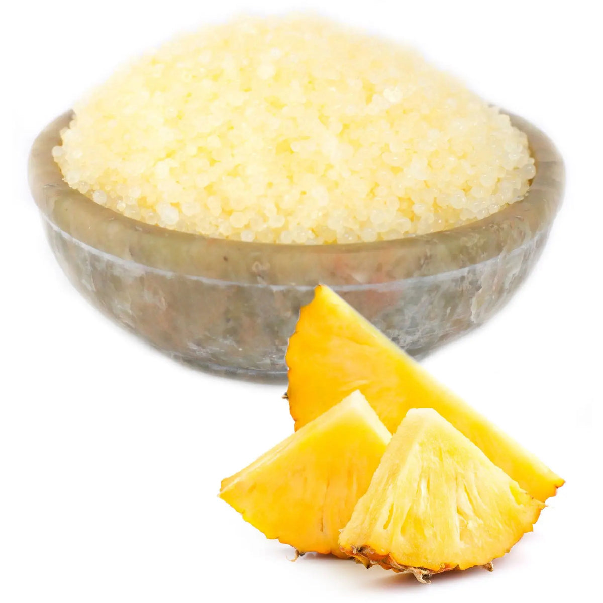 Cuenco gris con gránulos aromáticos amarillos, junto a trozos de piña fresca sobre fondo blanco.