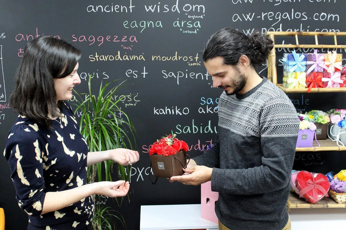 Un hombre entrega una caja cuadrada con un ramo de flores de jabón rojas a una mujer en una tienda.