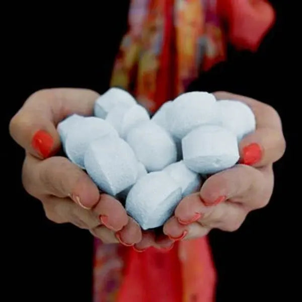 Manos sosteniendo un puñado de mini bombas de baño efervescentes de color blanco con forma de pastilla redondeada.