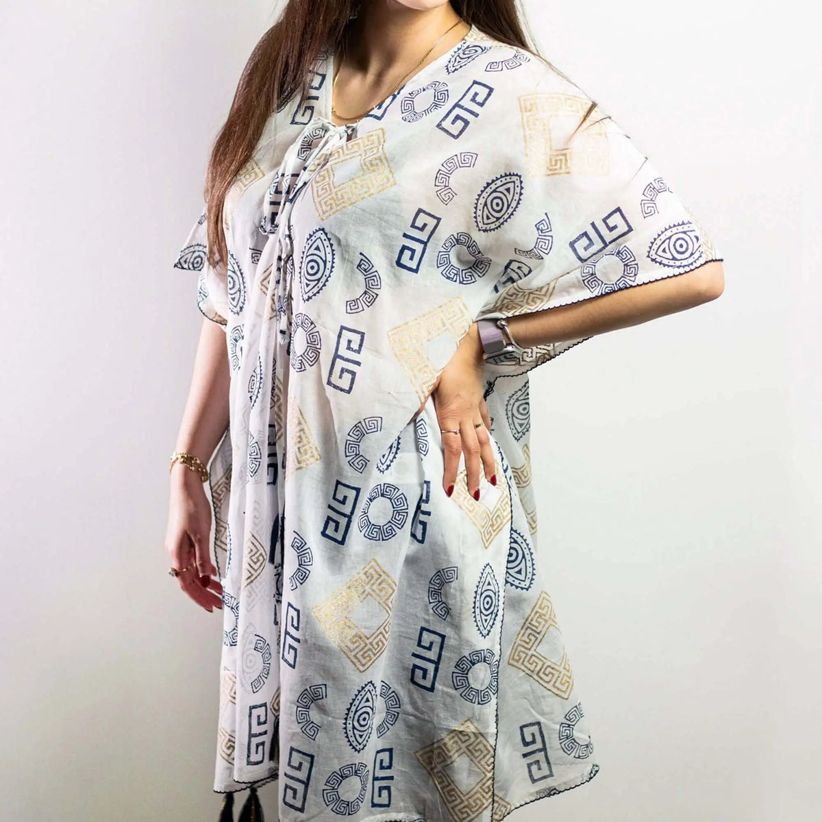 Kaftán blanco con estampados griegos y de ojos en azul y oro, corte amplio y ligero sobre una mujer.