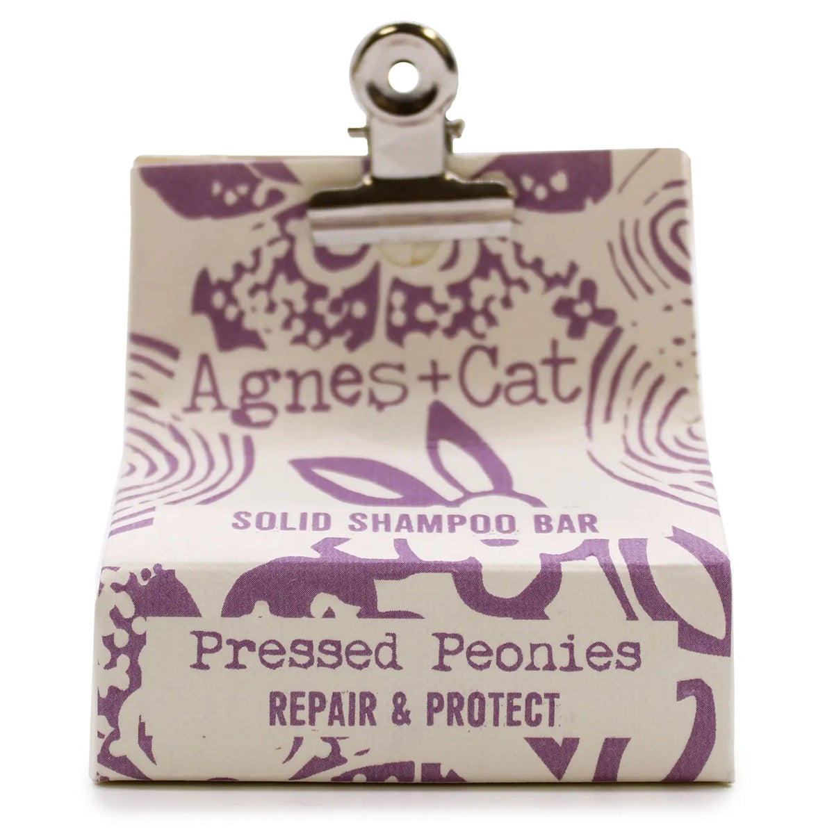 Champú sólido Agnes+Cat Peonías en caja de papel crema con diseño floral morado, sujeta con una pinza metálica.