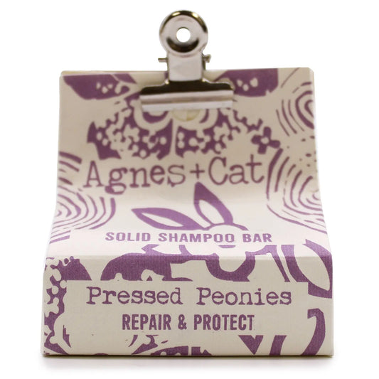 Champú sólido Agnes+Cat Peonías en caja de papel crema con diseño floral morado, sujeta con una pinza metálica.