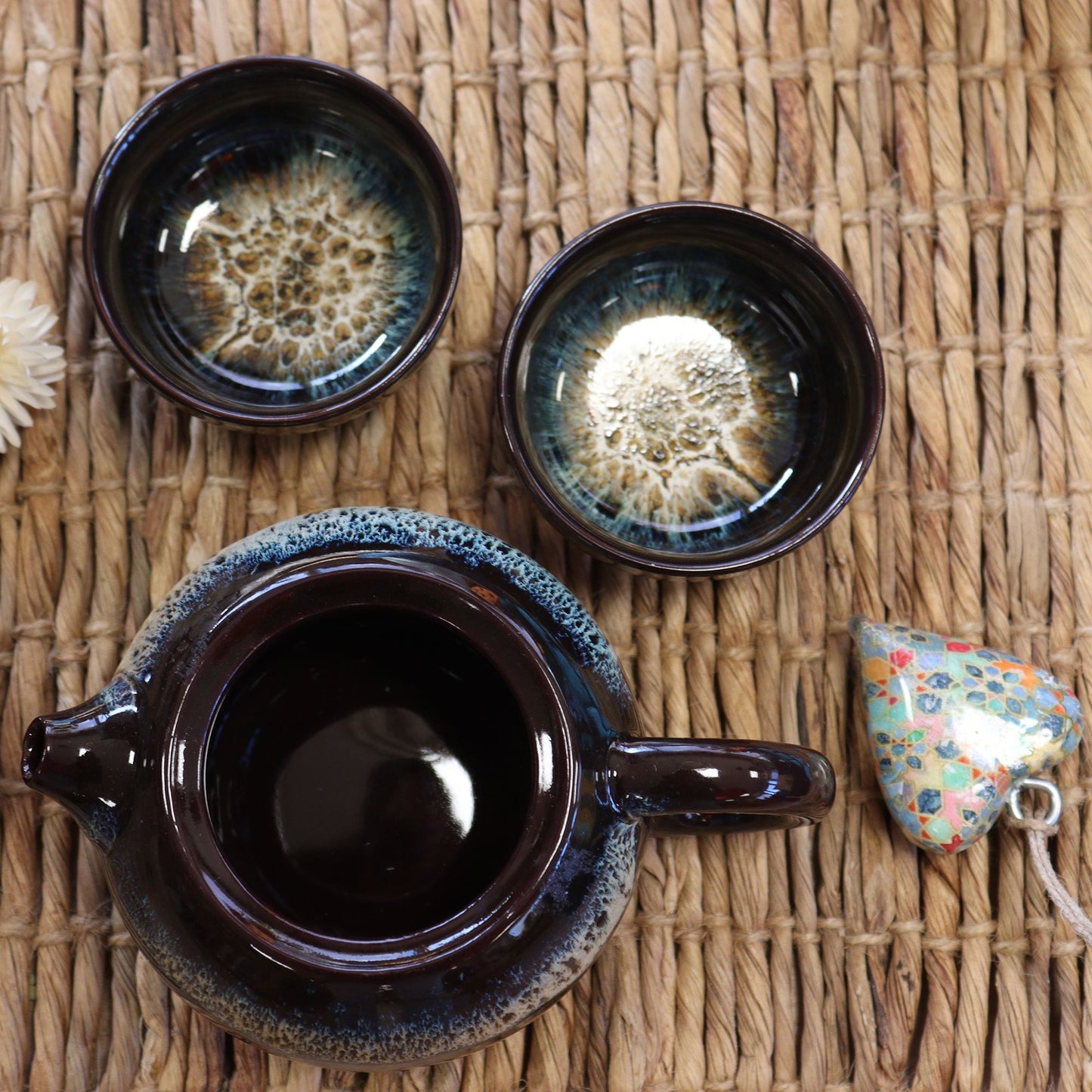 Juego de té en cerámica esmaltada negra con destellos azules sobre fondo de mimbre con una tetera y dos tazas a juego
