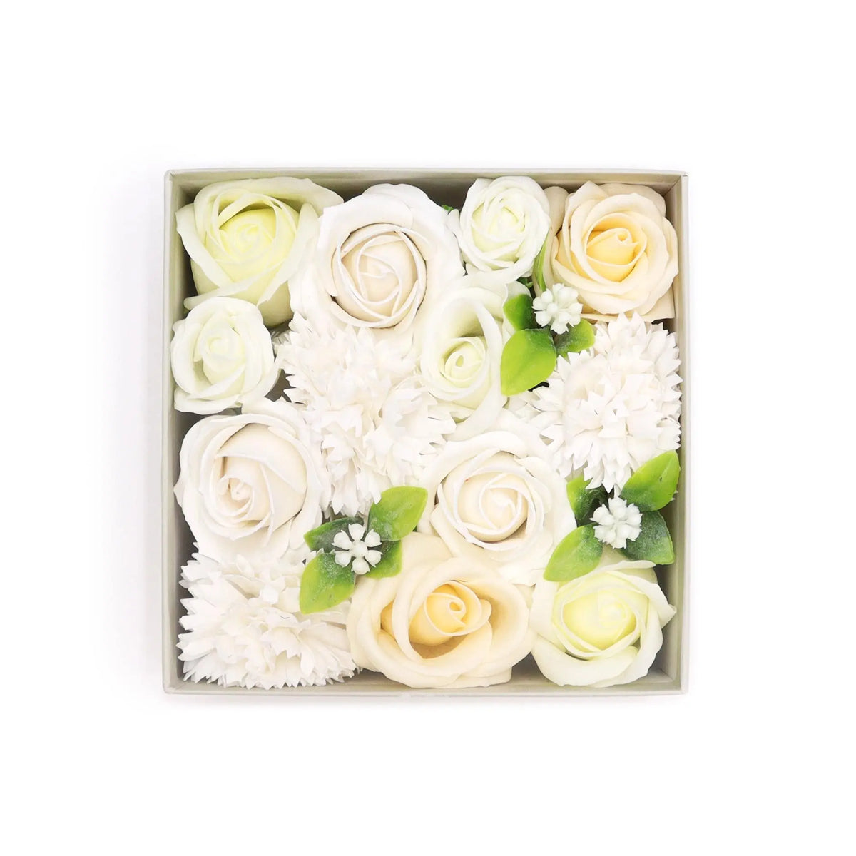 Caja cuadrada con flores de jabón en tonos blanco y marfil, decorada con hojas verdes y detalles florales pequeños.