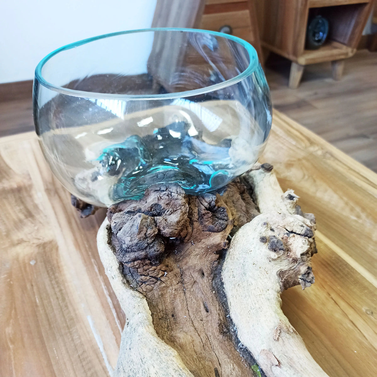 Cuenco de vidrio fundido transparente encajado sobre una base de madera rústica natural con vetas marcadas.