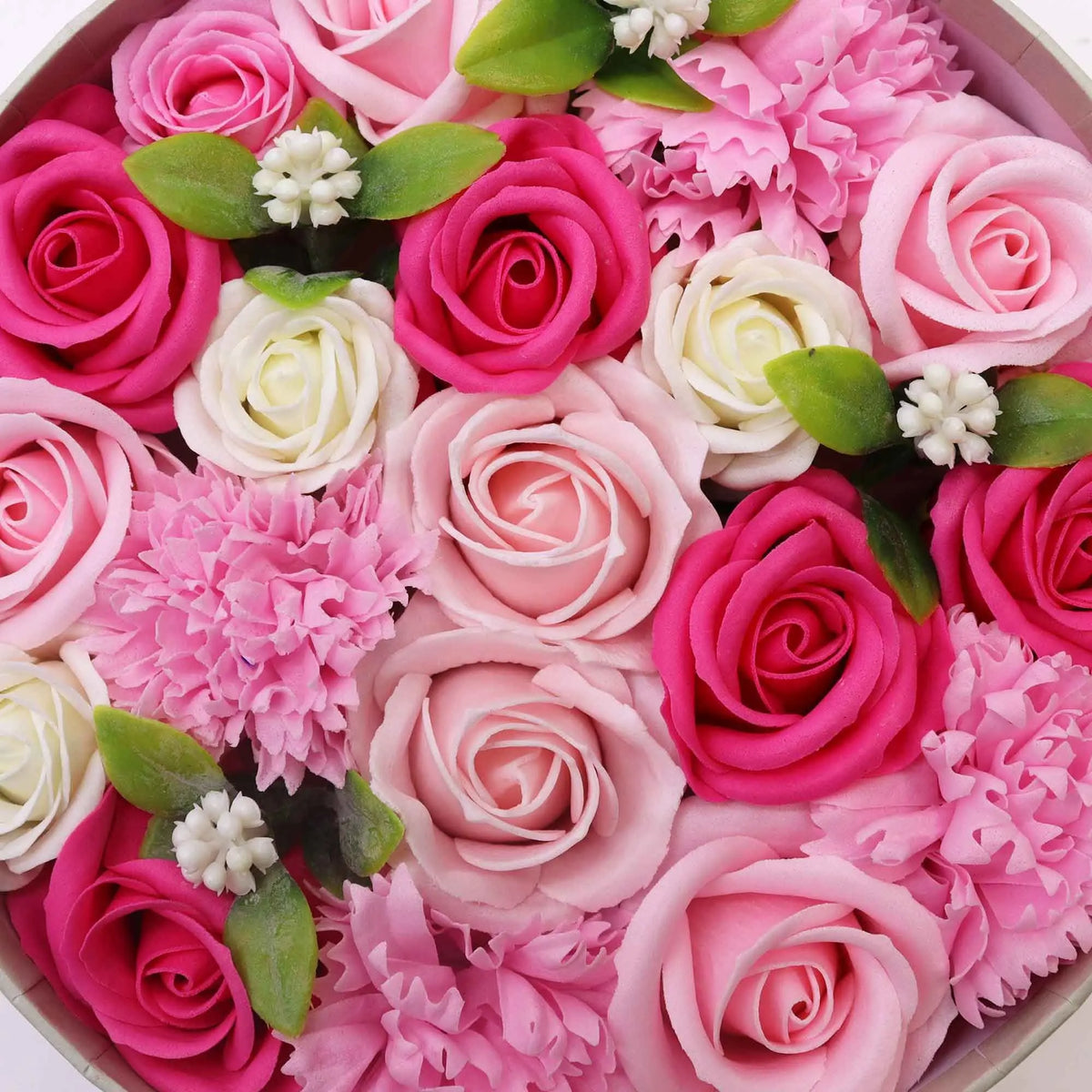 Caja redonda llena de flores de jabón en tonos rosa, blanco y fucsia, con hojas verdes y detalles decorativos.