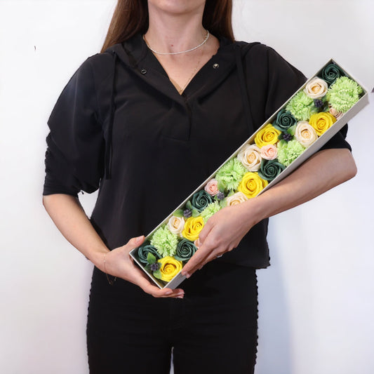 Caja rectangular extra larga con flores de jabón en tonos amarillo, crema y verde, sostenida por una persona.