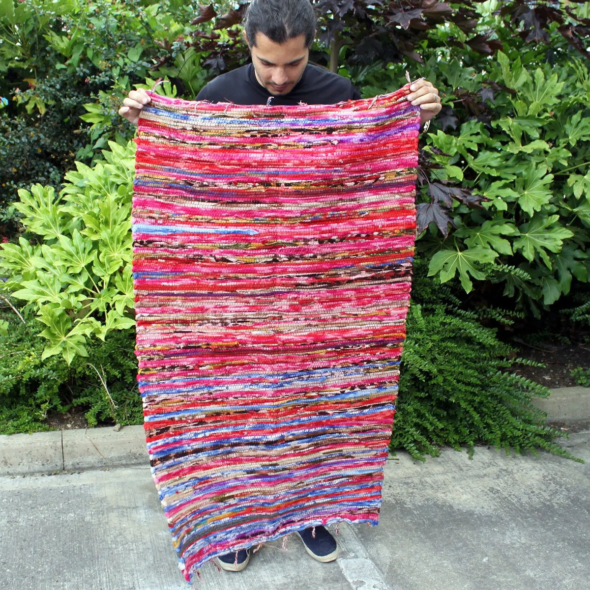 Alfombra de trapo artesanal, rectangular (128x75cm), con rayas horizontales multicolores en tonos rojizos y azules.