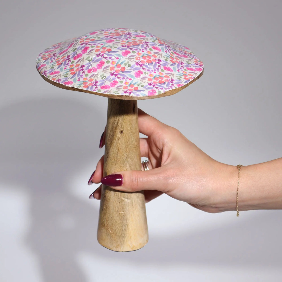 Seta decorativa de madera con sombrero esmaltado con estampado floral en tonos rosas y lilas, sostenida por una mano.