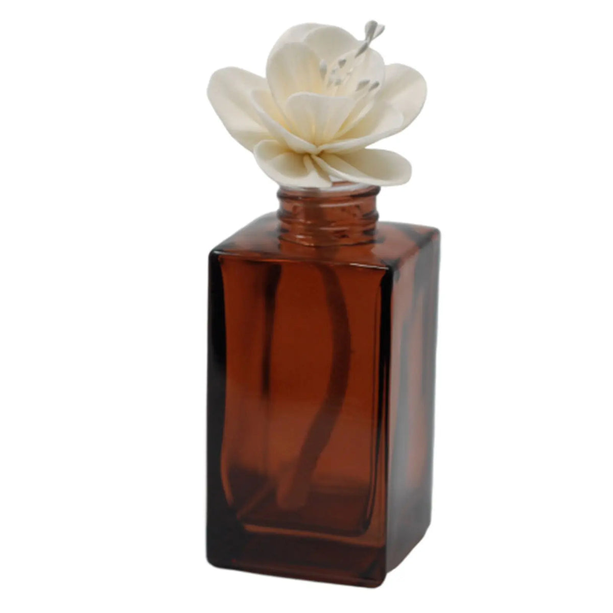Flor de loto de madera sola sobre frasco difusor de vidrio ámbar rectangular.