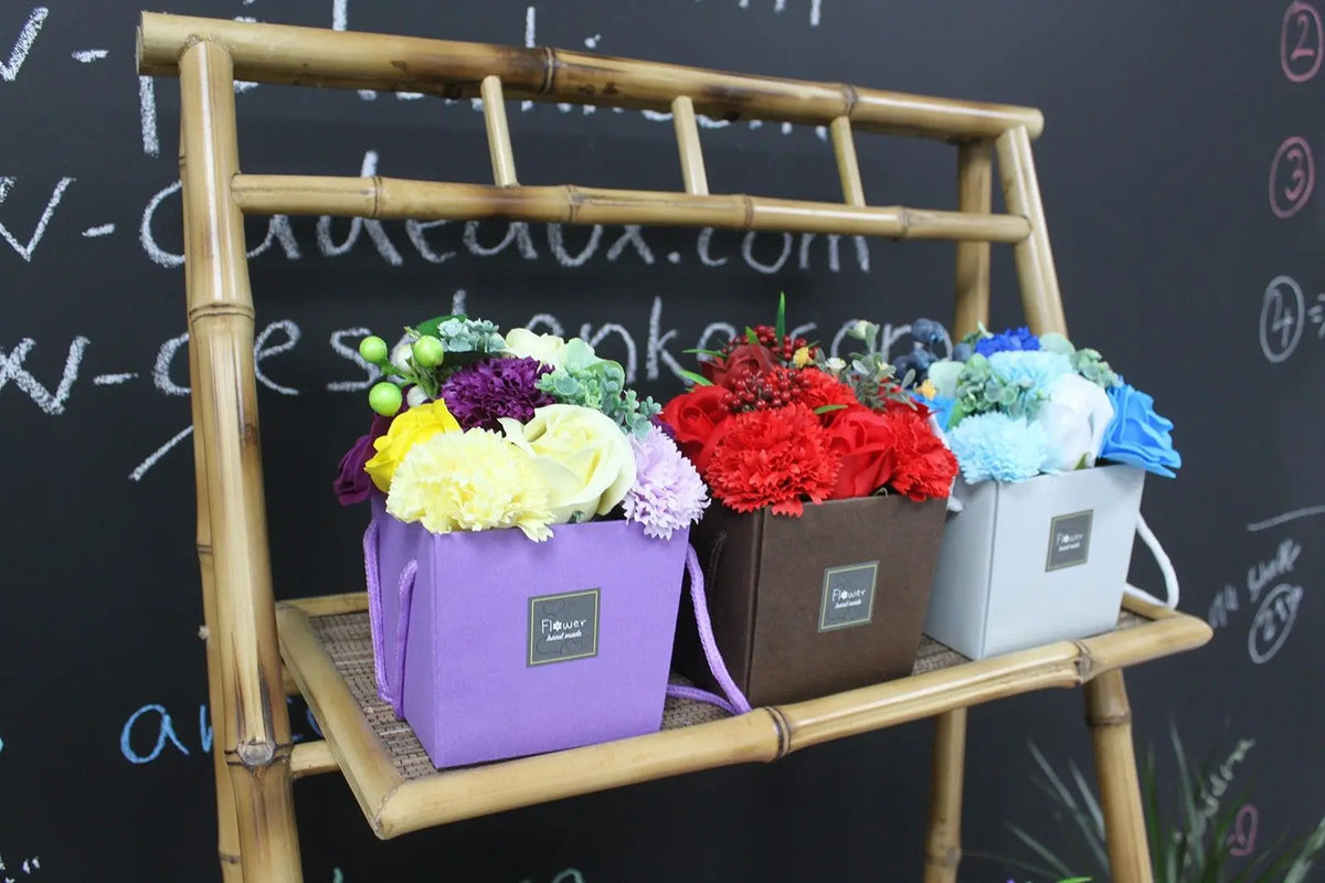 Tres cestas cuadradas con flores de jabón de colores (amarillo, rojo, azul) sobre un estante de bambú.