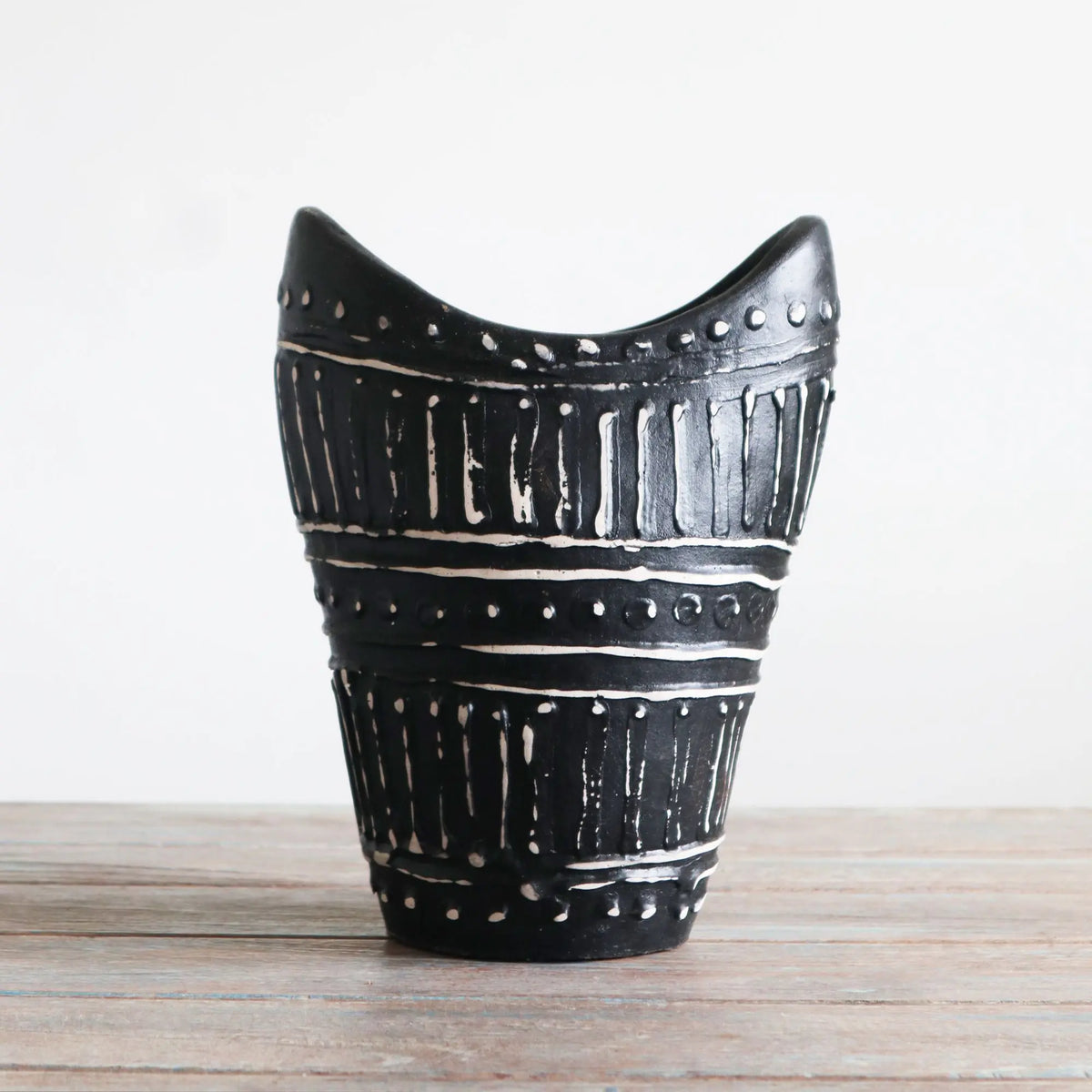 Jarrón de cerámica negro con relieve blanco, forma curva en la parte superior y diseño geométrico de líneas y puntos.