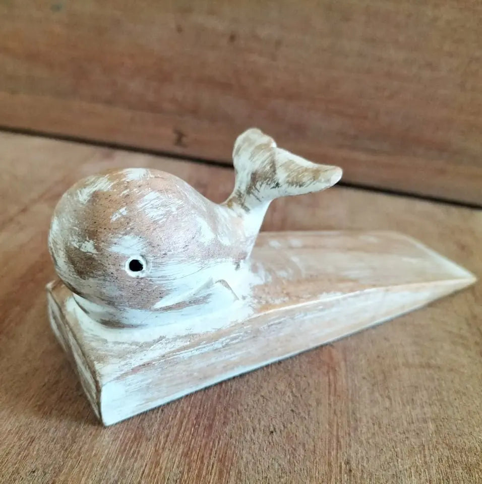 Tope de puerta de madera tallada en forma de ballena con acabado decapado en blanco y tono natural.