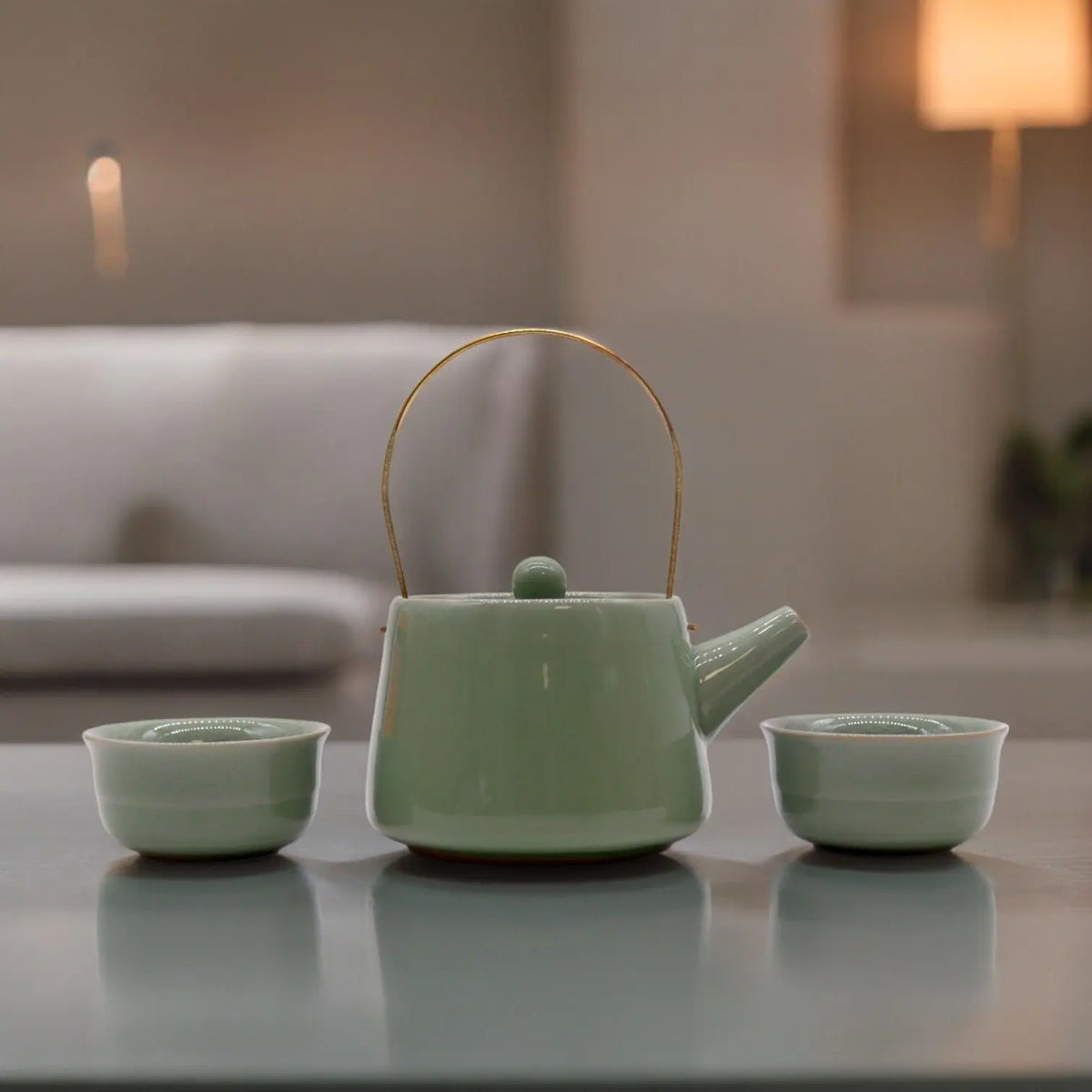 Set de té Ancient Wisdom: tetera cerámica verde con asa dorada y dos tazas a juego sobre mesa. Diseño minimalista.