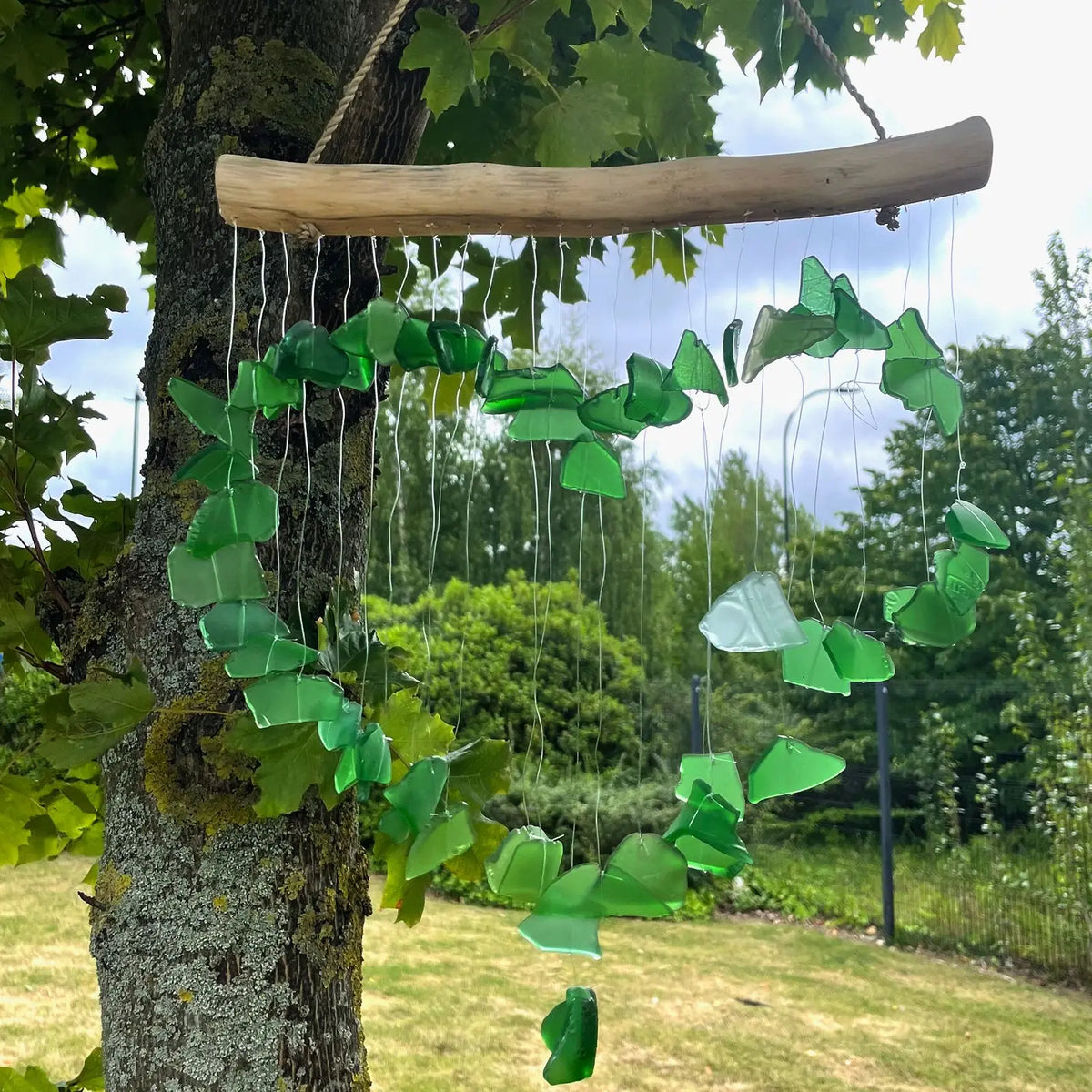 Carillón de piezas de vidrio reciclado verde y blanco colgando de una rama de madera, formando una silueta de corazón.