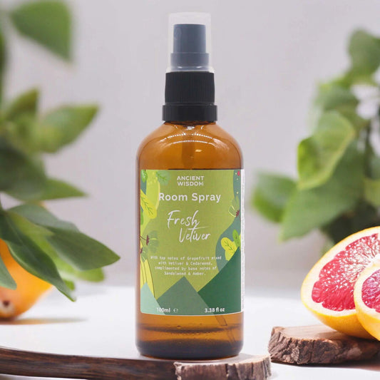 Ambientador en spray de 100ml, frasco de vidrio ámbar con etiqueta verde botánica, junto a pomelos y hojas frescas.