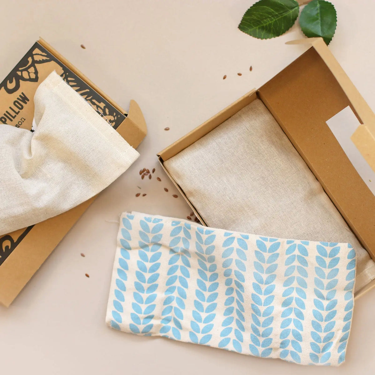 Almohada para ojos Agnes & Cat de tela beige con estampado de hojas azules, presentada en su caja de cartón artesanal.