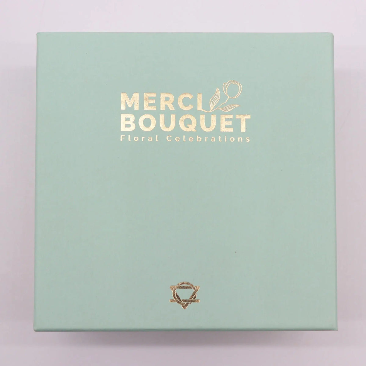 Caja regalo cuadrada de color verde menta con letras doradas y un pequeño logo en la parte inferior.