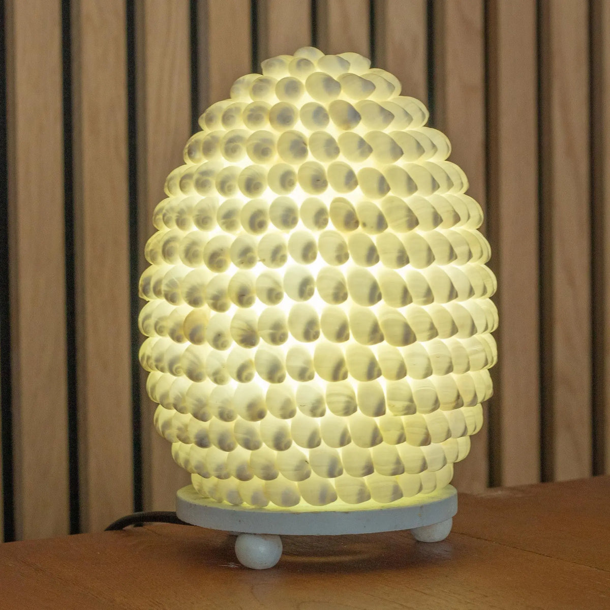 Lámpara boho ovalada de 15 cm, hecha con pequeñas conchas naturales blancas que emiten una cálida luz interior.