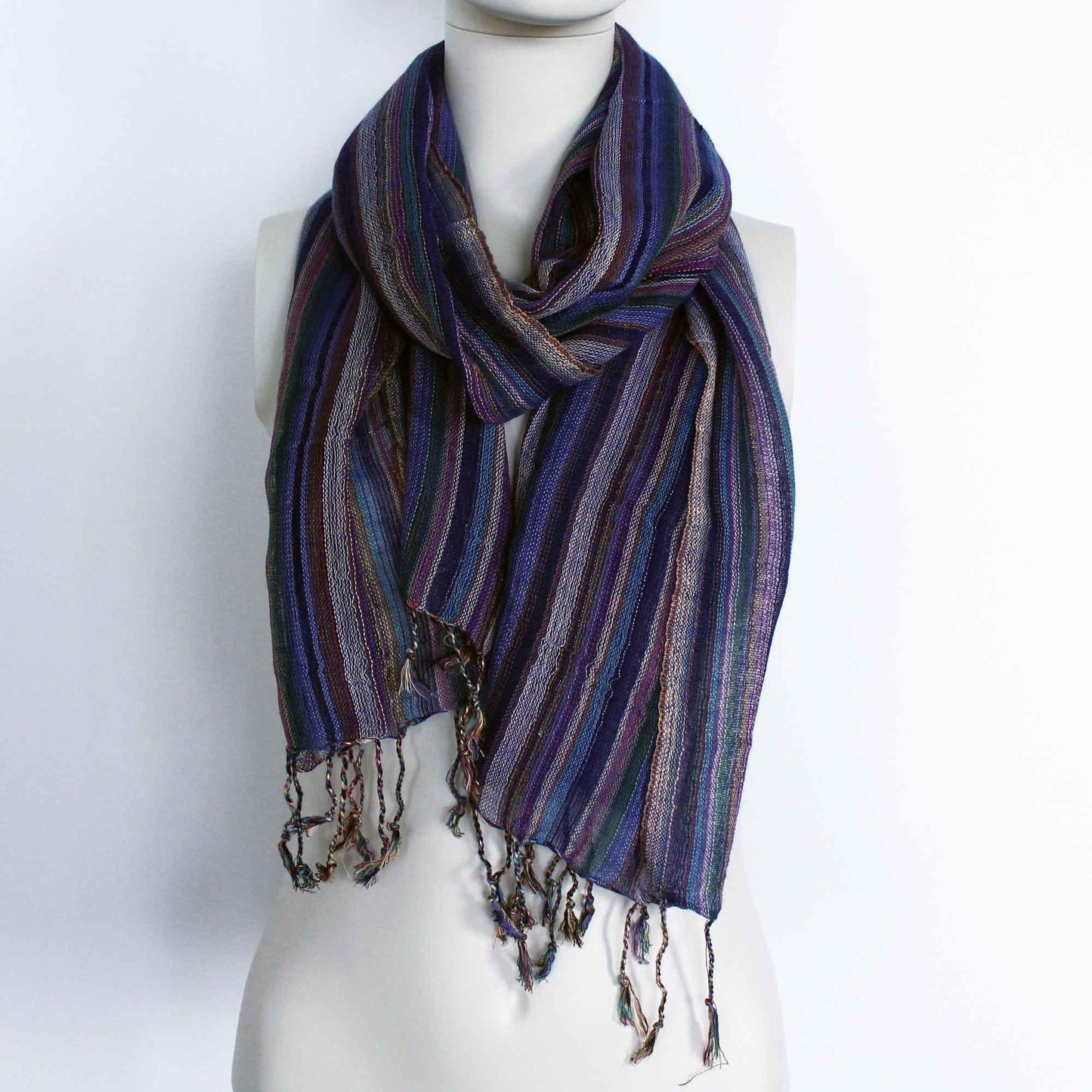 Bufanda bohemia a rayas azules y moradas con hilos dorados brillantes y flecos en los extremos sobre maniquí blanco.