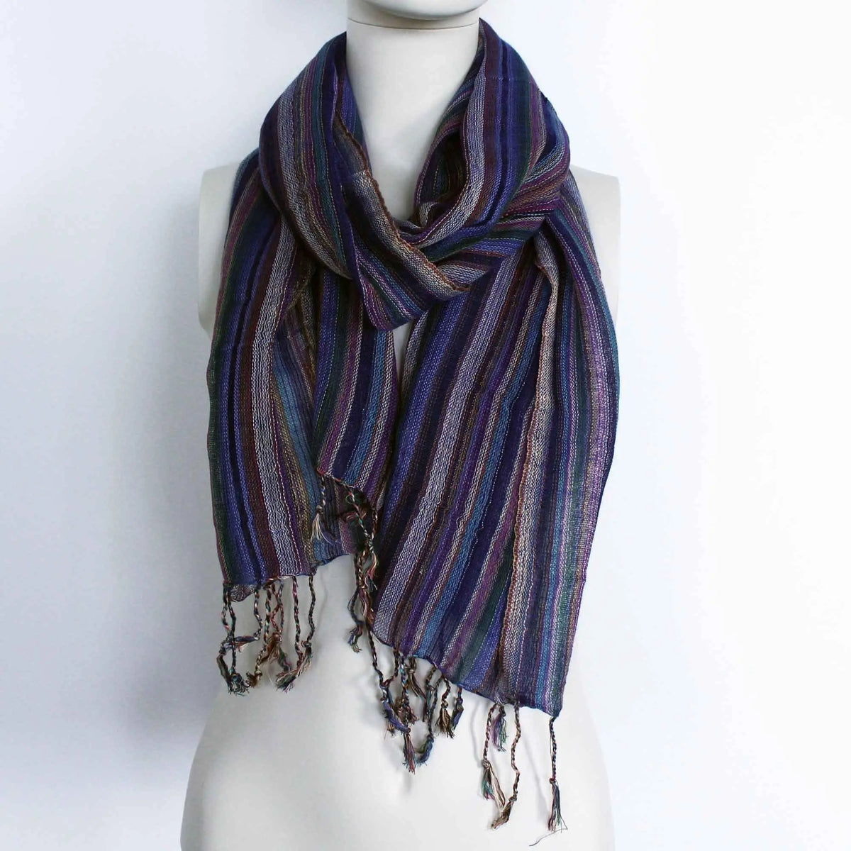 Bufanda bohemia a rayas azules y moradas con hilos dorados brillantes y flecos en los extremos sobre maniquí blanco.
