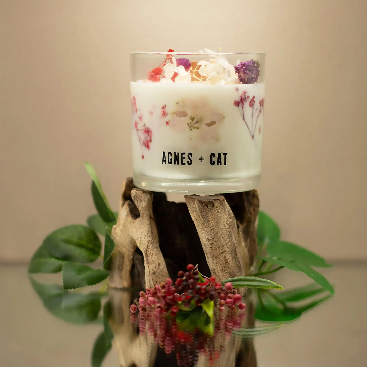 Vela aromática blanca con flores secas en vidrio, estilo elegante, marca Agnes + Cat, sobre soporte natural.