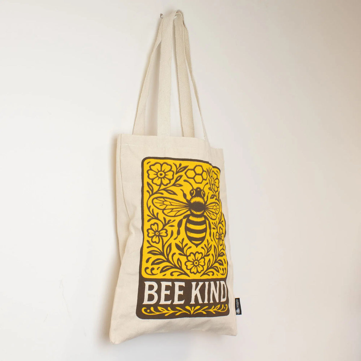 Bolsa de tela beige con diseño amarillo de abeja y frase "BEE KIND" en estilo vintage. Ideal para compras ecológicas.