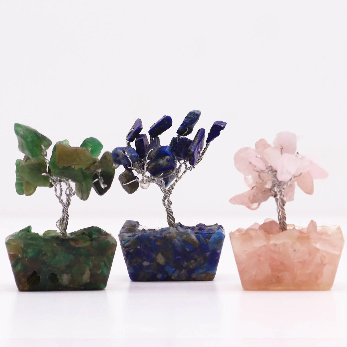 Tres mini árboles decorativos de alambre con hojas de piedras preciosas verde, azul y rosa sobre bases de orgonita.
