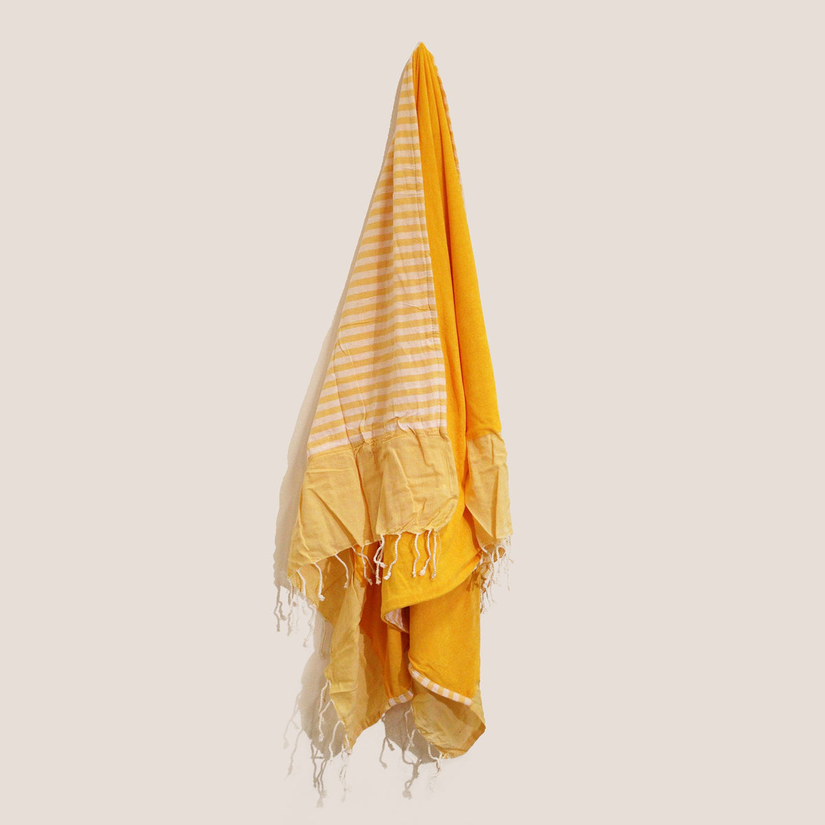 Toalla pareo de algodón amarillo, con diseño a rayas y flecos decorativos en los extremos, colgada verticalmente.