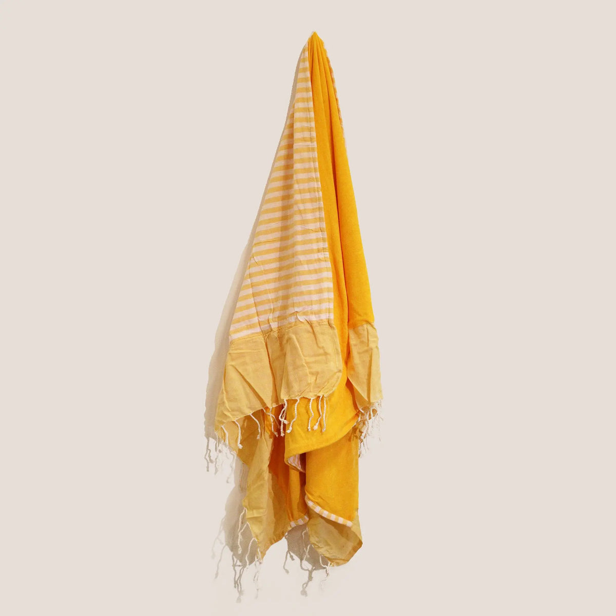 Toalla pareo de algodón amarillo, con diseño a rayas y flecos decorativos en los extremos, colgada verticalmente.