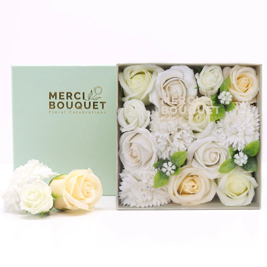 Caja cuadrada abierta con rosas y flores de jabón en tonos blanco y marfil, sobre un fondo verde menta.