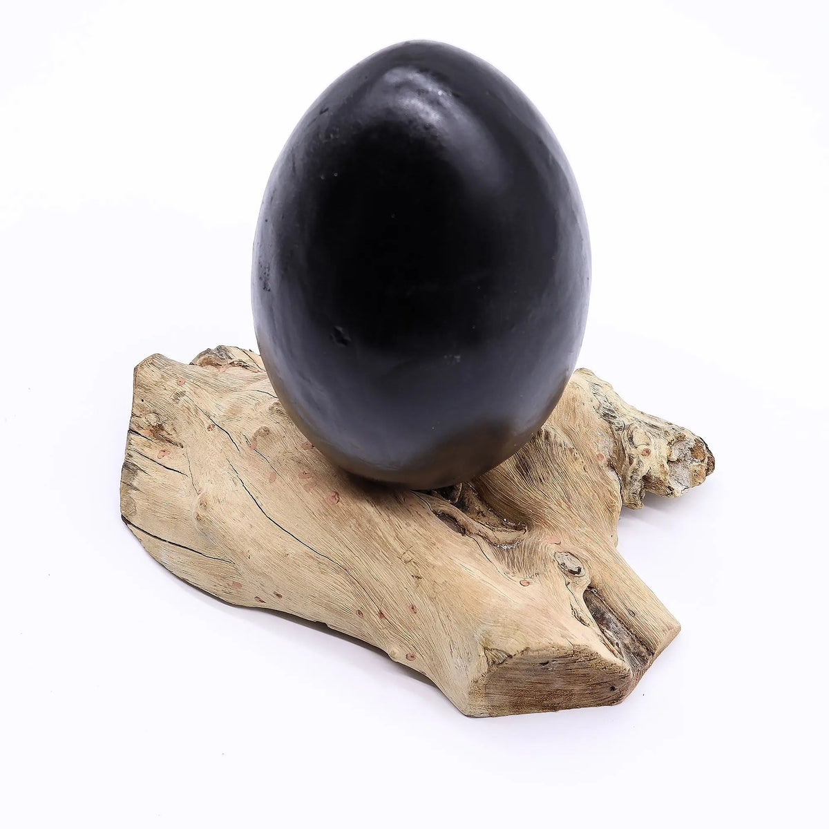 Lámpara de mesa con forma de huevo gris sobre una base de madera natural con texturas orgánicas.