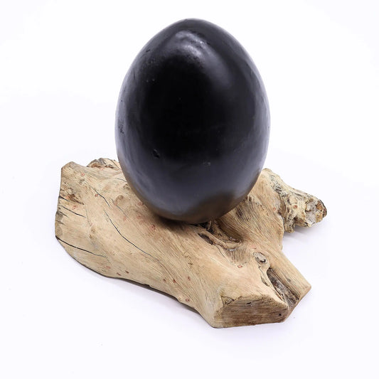 Lámpara de mesa con forma de huevo gris sobre una base de madera natural con texturas orgánicas.