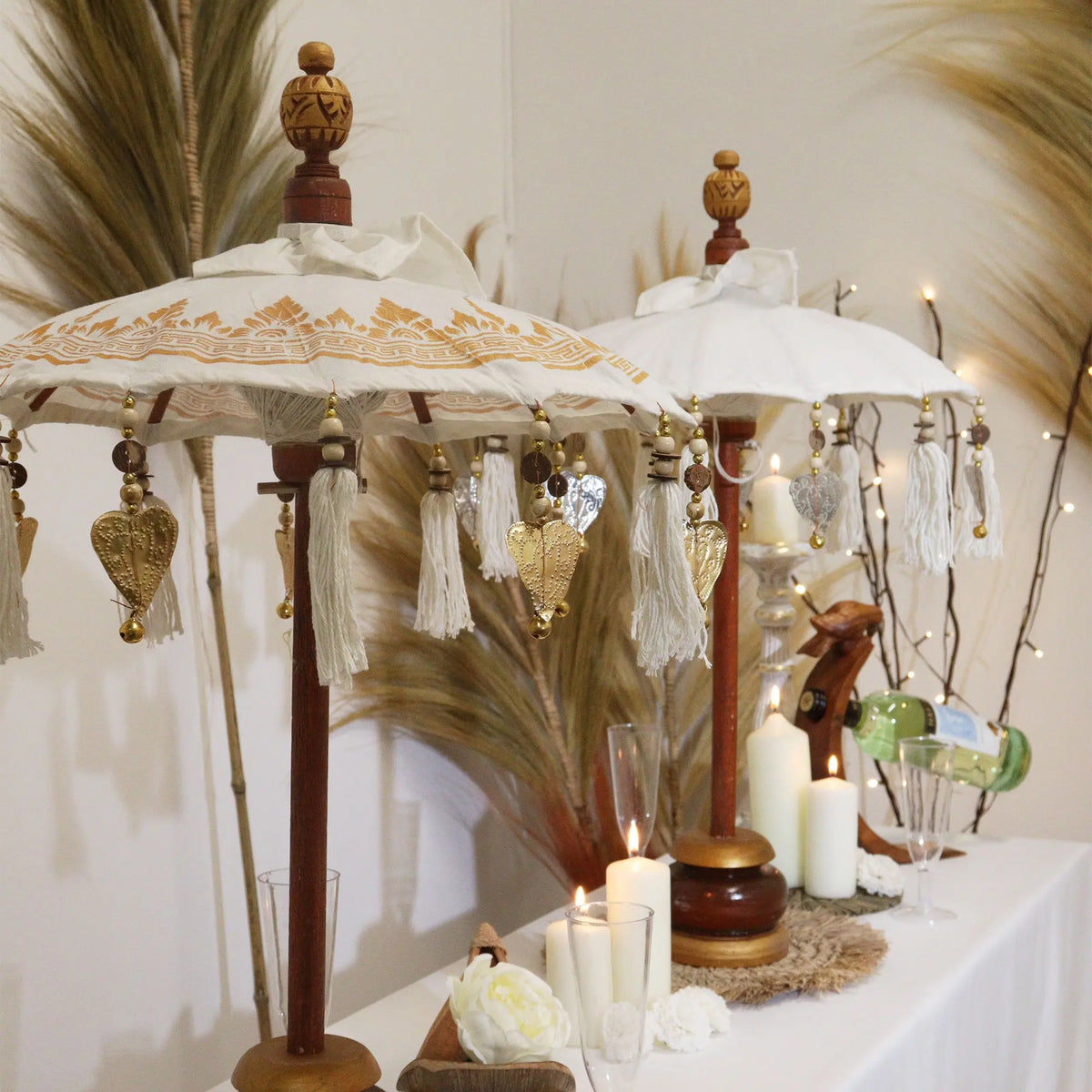 Sombrillas decorativas de Bali en lona blanca con detalles dorados, colgantes de corazón y mástil de madera artesanal.