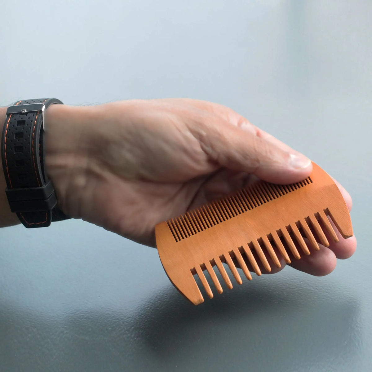 Mano sosteniendo peine de madera de doble cara Ancient Wisdom con dientes finos y anchos para el cuidado de la barba.