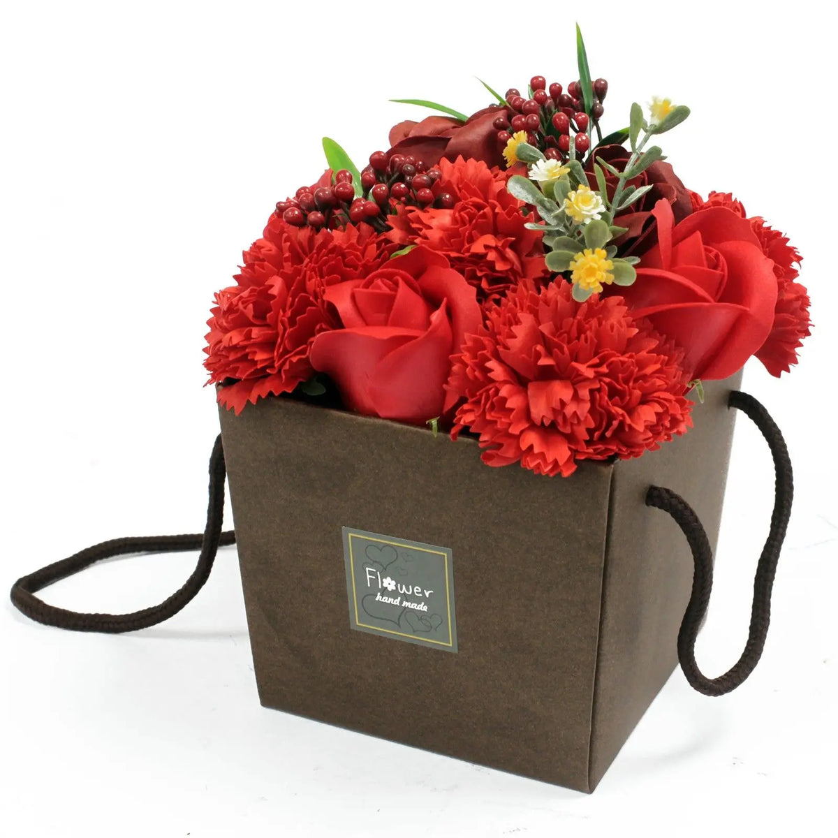 Bouquet de rosas y claveles rojos de jabón en una caja de regalo marrón con asas, sobre fondo blanco.