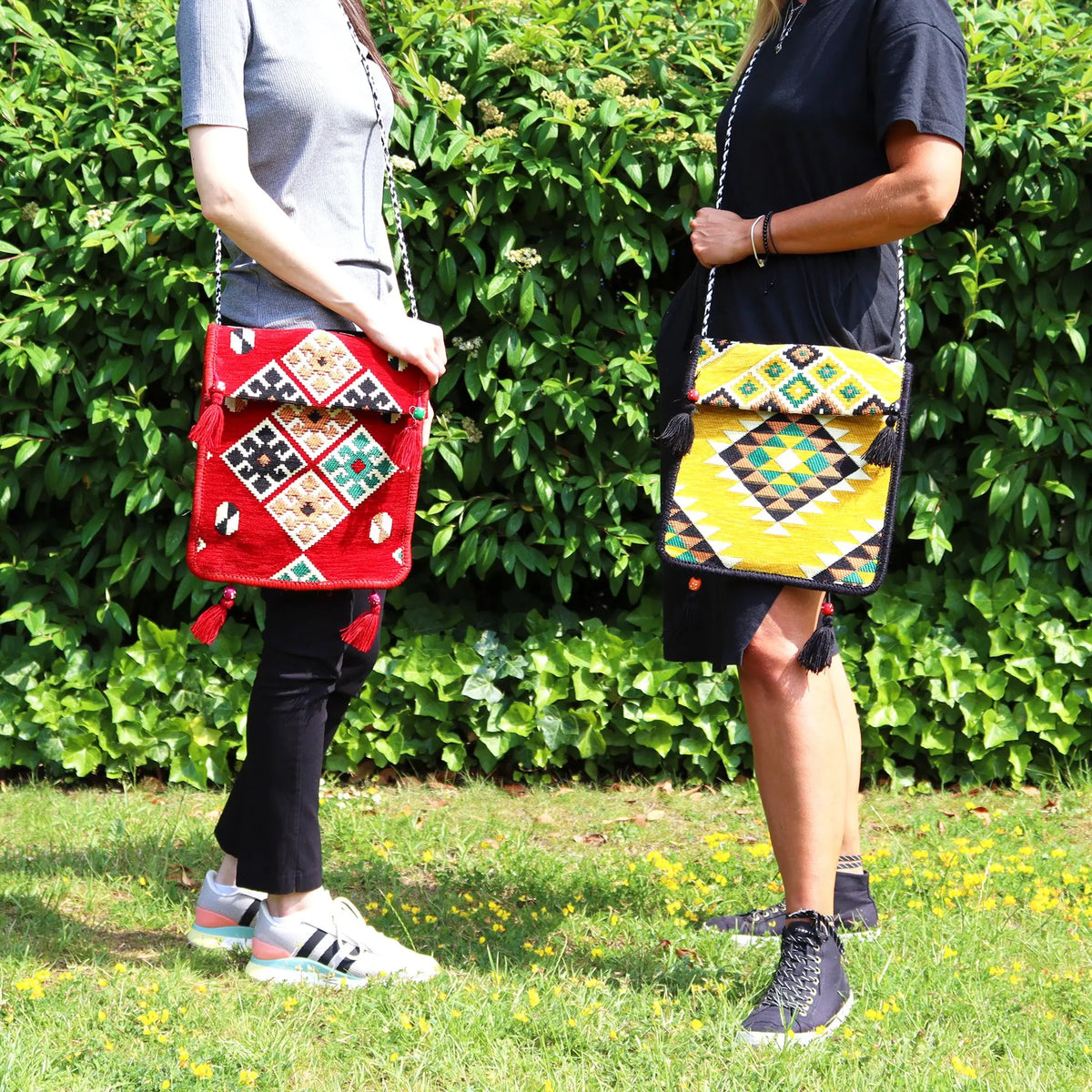 Dos bolsos bandolera de kilim con patrones geométricos, uno rojo y otro amarillo, con borlas y correa larga al hombro.