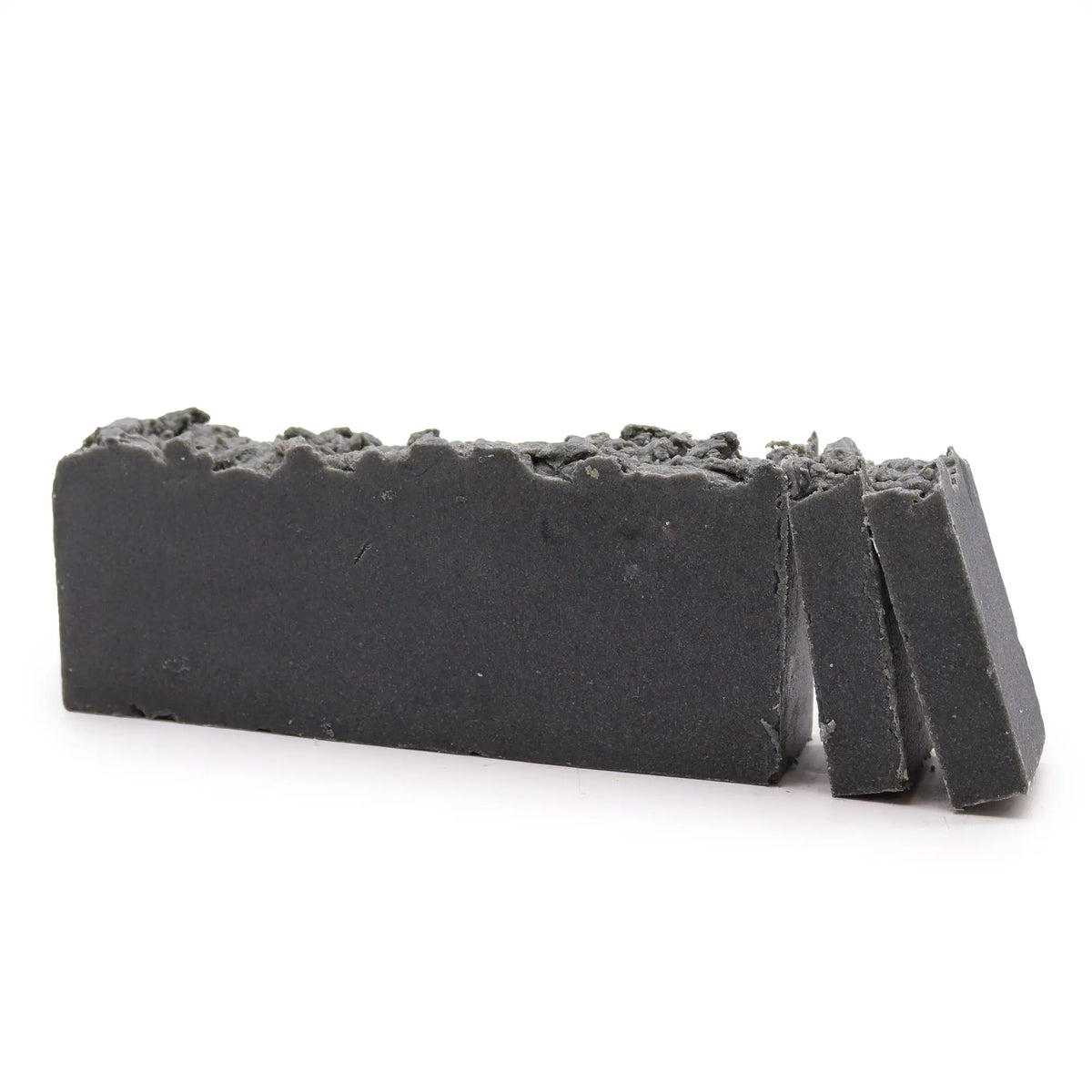 Barra de jabón artesanal exfoliante color gris oscuro con textura rústica sobre fondo blanco