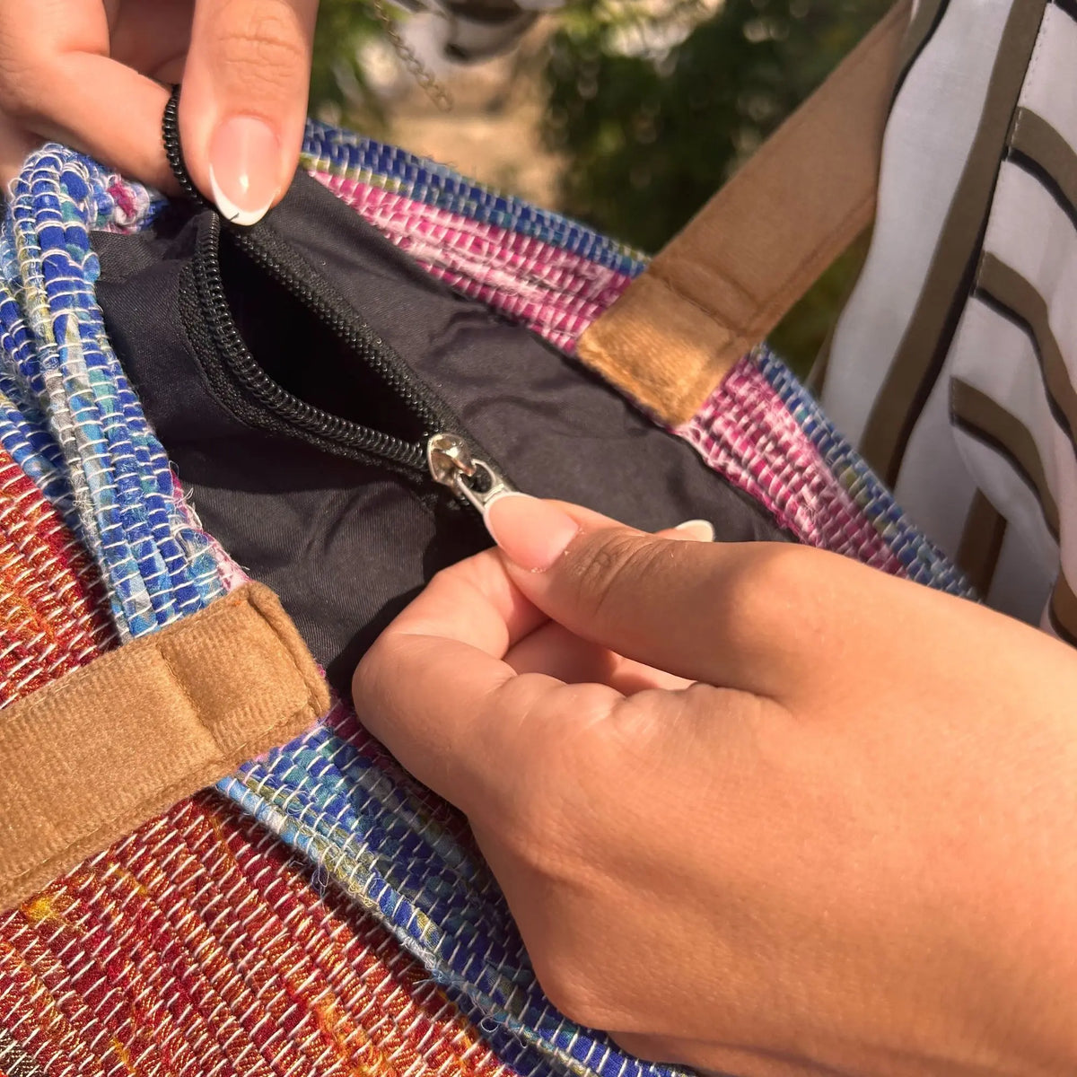 Bolso de tapete reciclado en tonos lavanda y rojo, con asas de gamuza café y bolsillo interno con cierre negro.