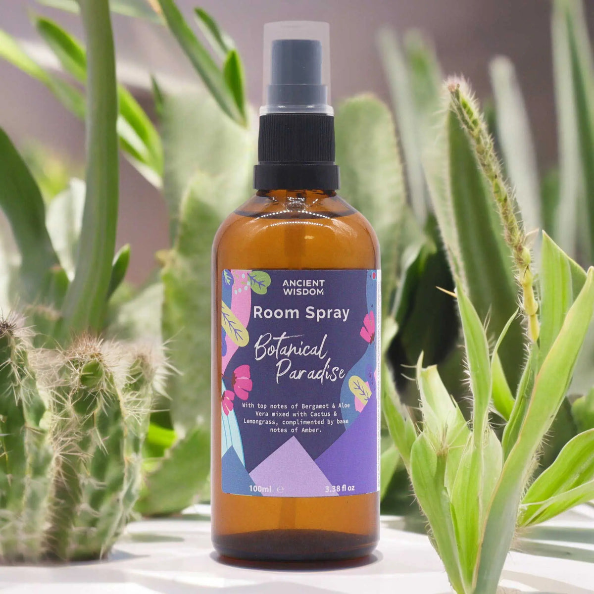 Spray ambientador de 100ml en botella de vidrio ámbar, con etiqueta floral colorida rodeado de cactus y plantas verdes.