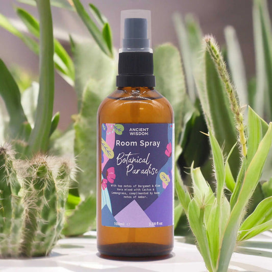 Spray ambientador de 100ml en botella de vidrio ámbar, con etiqueta floral colorida rodeado de cactus y plantas verdes.
