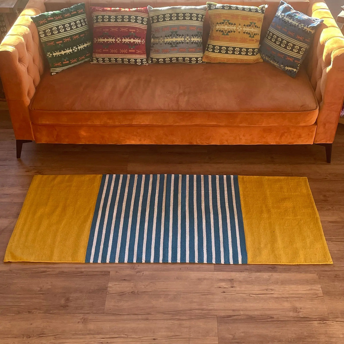 Alfombra de algodón rectangular con franjas verticales azules y blancas en el centro y laterales amarillos lisos.